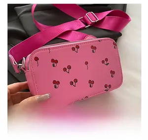 Detail showing the pink rectangular crossbody bag with cherry prints and silver hardware