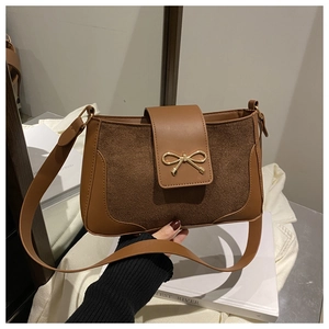 Detail of a brown suede shoulder bag with a metal bow buckle and smooth leather trim