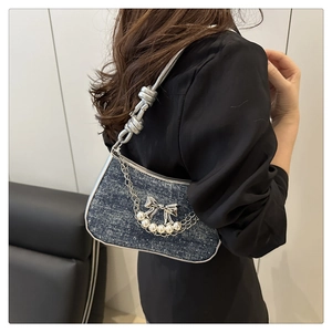 Detailed side view of denim shoulder bag with silver bow and pearl chain accessories