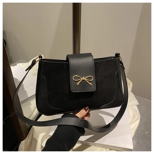Detail of a black crossbody bag with suede texture and golden bow-shaped metal clasp
