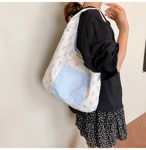 Detail of floral canvas tote bag featuring a blue plaid pocket with lace trim and bow patterns