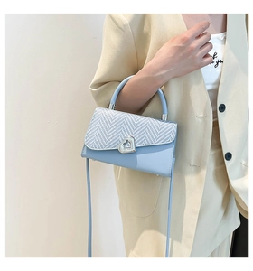 Detail of light blue crossbody bag featuring a silver heart-shaped clasp on woven texture