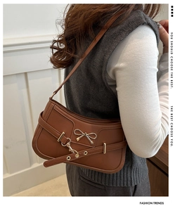 Detail of a brown faux leather shoulder bag featuring a metallic bow and eyelet strap