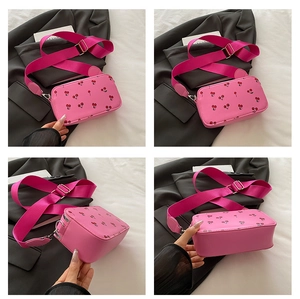 Detail view of pink cherry print crossbody bag with fuchsia wide strap and silver hardware