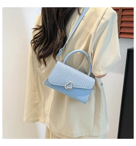 Detail of light blue crossbody bag featuring a silver heart buckle and woven flap texture