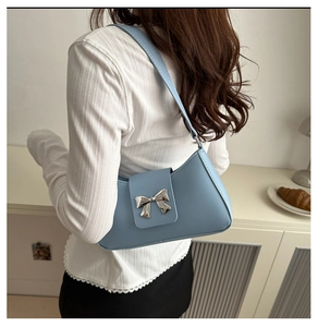 Detailed view of light blue underarm bag with silver bow buckle on model shoulder