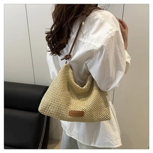 Detail of hand-woven straw tote bag featuring brown leather strap and fashion label