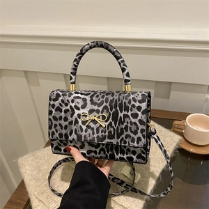 Retro leopard print mini crossbody bag with golden bow clasp on a wooden desk