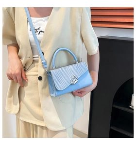 Crossbody view of light blue bag with woven texture flap and silver heart buckle