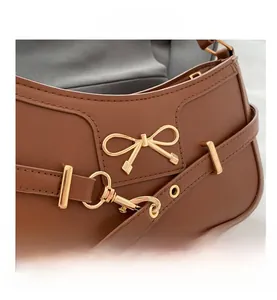 Detail of brown leather underarm bag with gold bow hardware and adjustable strap
