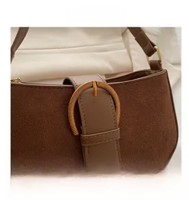 Detail of brown suede shoulder bag with golden spiral textured metal buckle and smooth leather