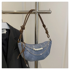 Dettaglio borsa a mezzaluna in denim con catena di perle e tracolla in pelle annodata