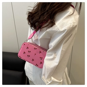 Pink crossbody camera bag with red cherry print and adjustable wide strap on a white shirt
