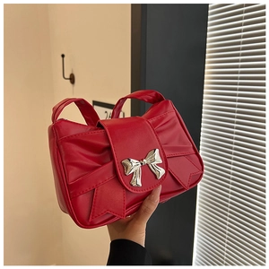 Close-up of red pleated handbag featuring a large silver metallic bow and textured PU leather
