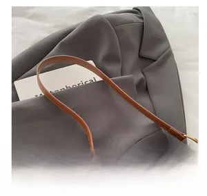 Close-up of brown leather bag handle with metal buckle on a grey suit jacket
