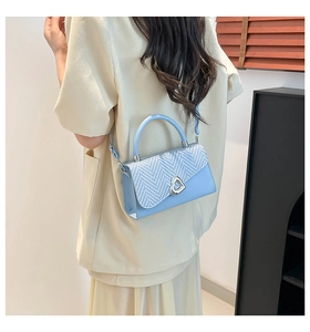 Detail of light blue crossbody bag featuring woven texture and heart-shaped metal clasp