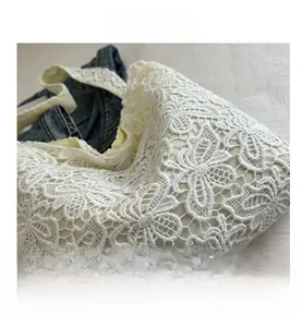 Gros plan sur la dentelle florale complexe et le tissu évidé d'un sac cabas blanc cassé