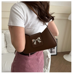 Detailed view of silver bow buckle on vintage brown shoulder bag worn by model