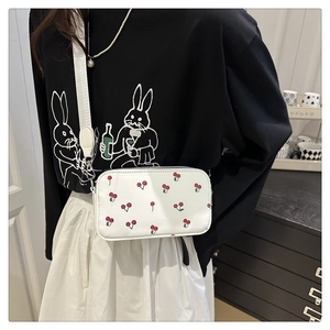 Détail d'un sac bandoulière blanc à motif cerise porté sur une tenue décontractée
