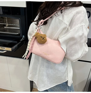 Detailweergave van de roze maanvormige tas met gevlochten riem en een beer hanger