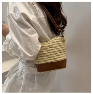Detail of straw bucket bag featuring brown leather base and matching shoulder strap