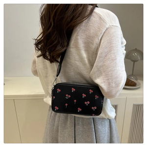 Detail view of black crossbody bag with cherry print worn by a model in minimalist interior