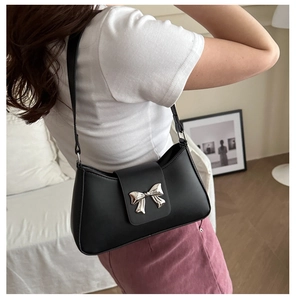 Detail view of black underarm bag with a silver metal bow buckle on a leather strap
