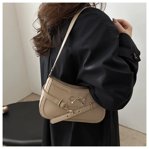 Detail of a beige leather shoulder bag with a gold bow buckle worn over a black trench coat