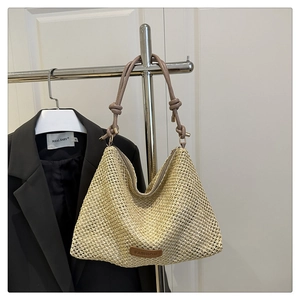 Detail of hand-woven beige straw tote bag with brown leather handles and fashion label