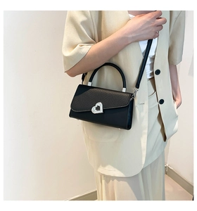 Detail of vintage black crossbody bag with silver heart buckle on a beige suit model