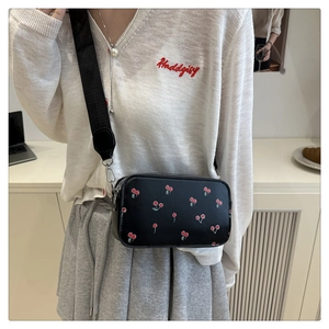 Détail d'un sac bandoulière noir avec imprimé cerise et large sangle porté par un mannequin