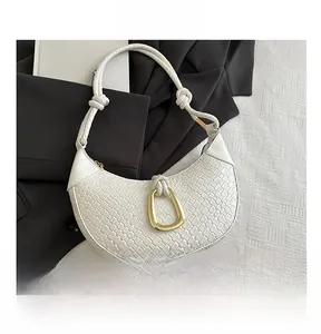 Close-up of white woven half-moon bag featuring a knotted handle and golden D-ring
