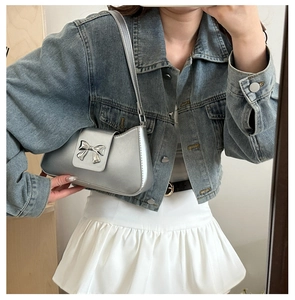 Silver shoulder bag with metallic finish and bow detail worn by a model