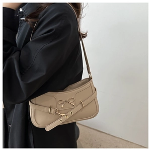 Détail d'un sac à bandoulière beige avec nœud doré et sangle à œillets réglable