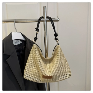 Detail of woven straw tote bag with black rope handles and brown leather fashion label