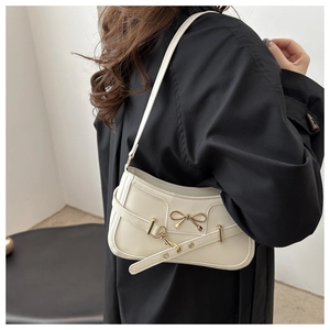 Detail of a chic cream underarm bag with a golden bow buckle shown on a model