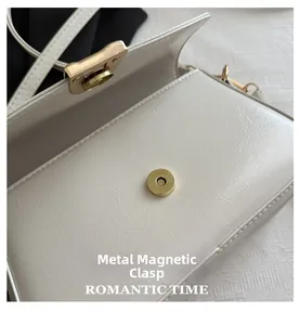 Gros plan détaillé de la boucle magnétique dorée sur un sac à main en cuir blanc
