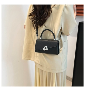 Detail of black crossbody bag with silver heart buckle worn by model on plain background