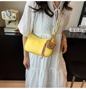 Detail of yellow crescent shoulder bag featuring a cute brown plush bear charm and PU leather