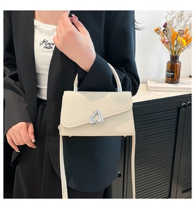 Detail of cream bag featuring woven texture flap and silver heart-shaped rotary clasp