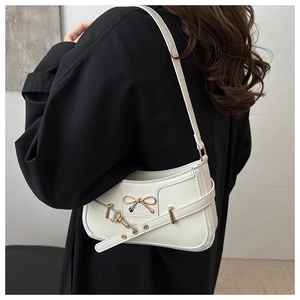 Close-up of white shoulder bag featuring a golden bow buckle and decorative leather strap