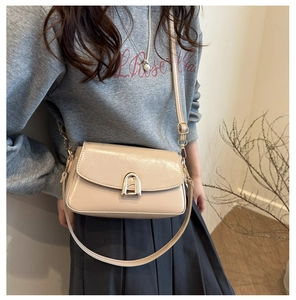 Détail du sac à bandoulière beige brillant avec un fermoir en métal doré de forme arquée
