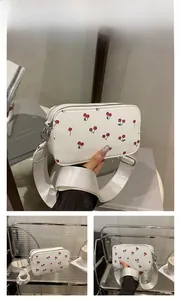Close-up of small white PU leather crossbody bag featuring cute red cherry print details