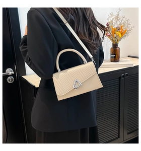 Detail showing the creamy beige textured woven flap and silver heart-shaped metal twist lock