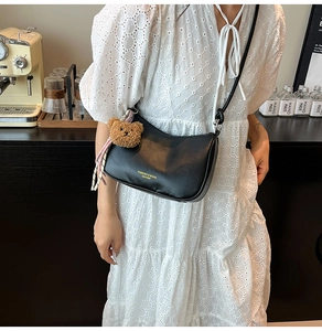 Detail of black leather shoulder bag with bear charm and golden logo on the bottom