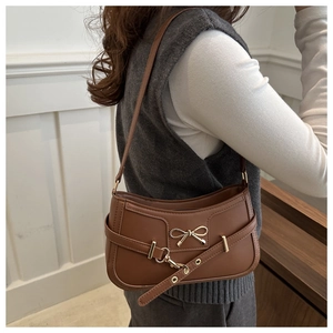 Détail d'un sac porté épaule marron avec boucle nœud dorée et sangle décorative en cuir