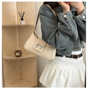 Detail of a creamy white underarm bag with a silver bow decoration and slim shoulder strap