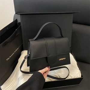 Bolso bandolera negro minimalista con logo dorado en caja de regalo de lujo