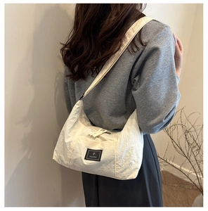 Close-up of the beige nylon hobo bag featuring a black brand tag and pleated texture