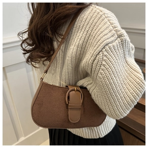 Detail of a brown suede baguette bag with vintage oval buckle on a knit sweater